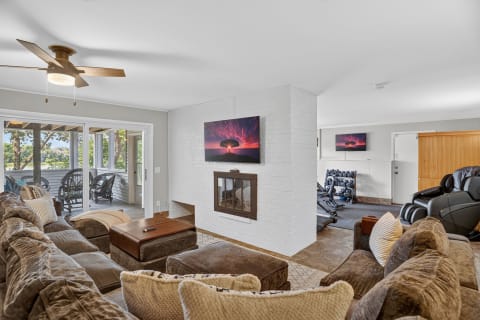 A spacious living room with a sectional sofa, fireplace, and fitness equipment, surrounded by natural light from glass doors.
