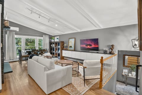 A modern living room with soft seating, large windows, and an open layout, featuring a stylish coffee table and a dining area.