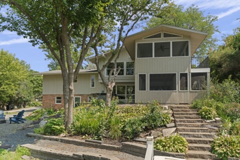 Exterior of a mid-century modern home surrounded by trees and terraced landscaping leading to the entrance.
