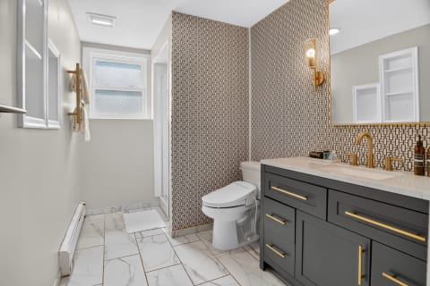 Contemporary bathroom with dark vanity, marble flooring, and geometric wallpaper.