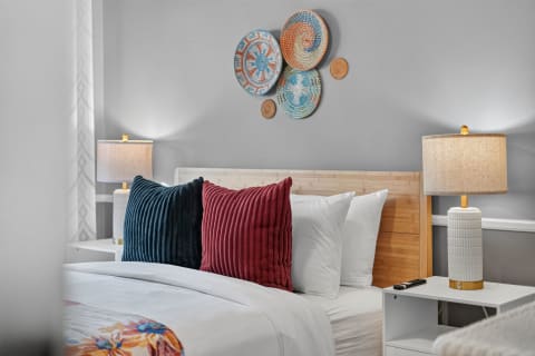 Serene bedroom with white linens, colorful pillows, and decorative woven baskets on the wall.