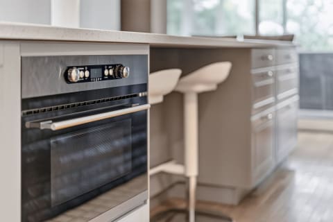 Modern kitchen view showcasing an oven, countertop, and white bar stools.