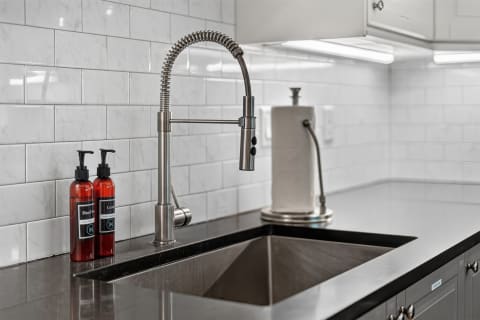 Modern kitchen sink featuring a stainless steel faucet and stylish hand soap and lotion bottles against a white subway tile backdrop.