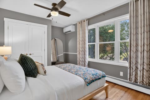 Elegant bedroom featuring gray walls, a comfortable bed with a colorful throw, and bright garden views through large windows.