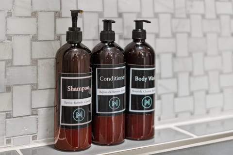 Three amber bottles labeled shampoo, conditioner, and body wash on a countertop with chic tile work in the background.