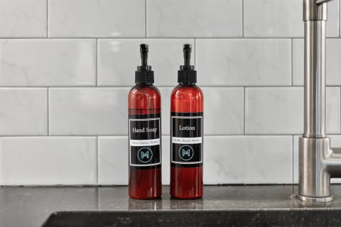 Two stylish bottles of hand soap and lotion on a sleek countertop, framed by white subway tiles.
