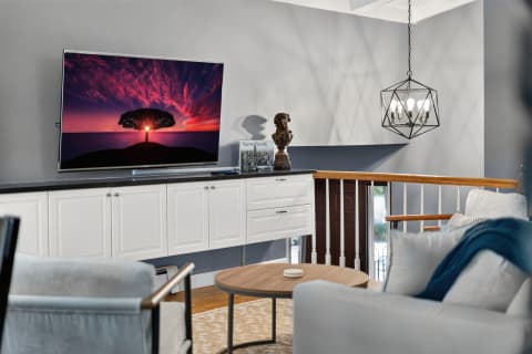 A modern living room with a sleek TV showing a sunset, elegant furniture, and a geometric chandelier overhead.