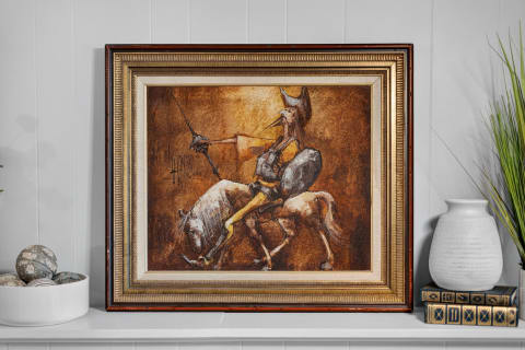 Framed wall art of a warrior on horseback above a shelf with a vase and decorative books.