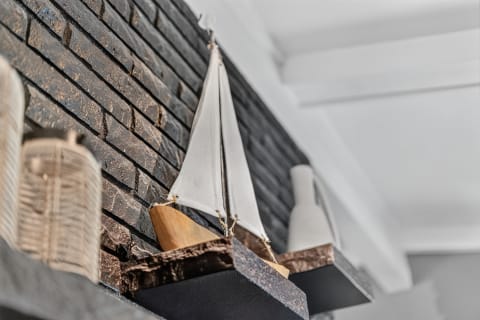 A handcrafted sailboat displayed on a dark brick wall shelf beside decorative vases, evoking a nautical theme.