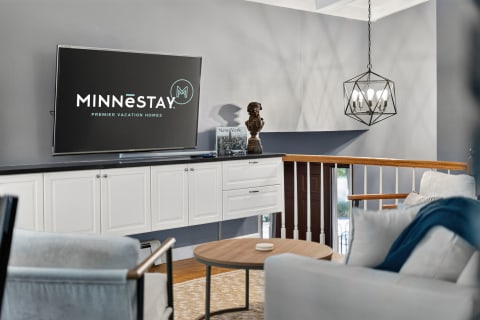 Modern living room displaying a TV, white cabinetry, stylish chandelier, and cozy seating area.