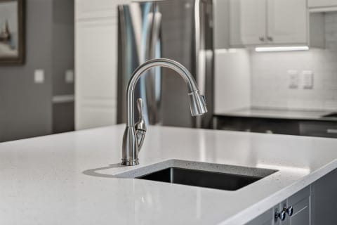 Close-up shot of a modern kitchen faucet on a white countertop with a black sink.