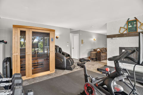 A private fitness area featuring a Peloton bike, sauna, and massage chair with a cozy sitting area in the background.