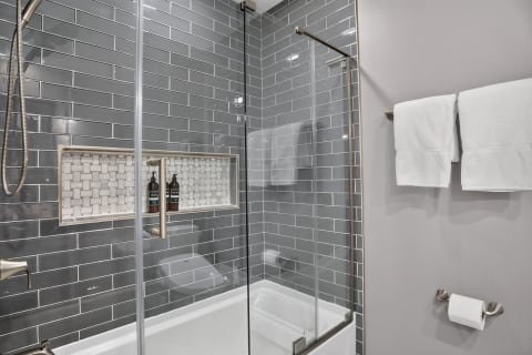 A modern shower featuring gray subway tiles, a glass enclosure, and neatly arranged towels.