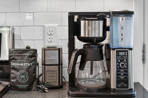 A Ninja Coffee Bar and a Cuisinart grinder on a kitchen countertop, accompanied by a package of Minnestay coffee.