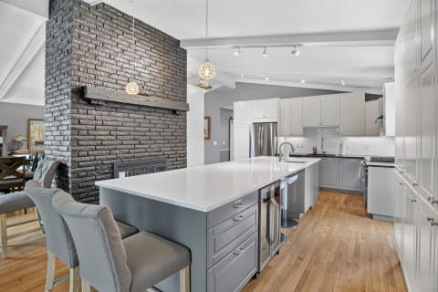 A spacious kitchen showcasing modern appliances, a quartz island, and a rustic black brick fireplace.
