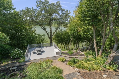 A landscaped garden with tiered pathways leading to a lakefront deck, lush greenery, and hydrangeas.