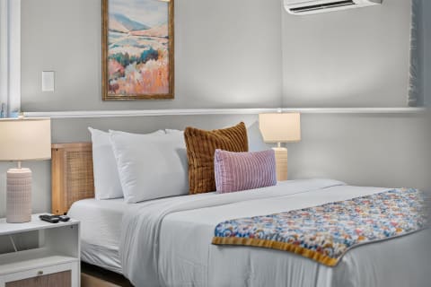 A cozy light-filled bedroom featuring a neatly made bed with colorful pillows and warm bedside lamps.