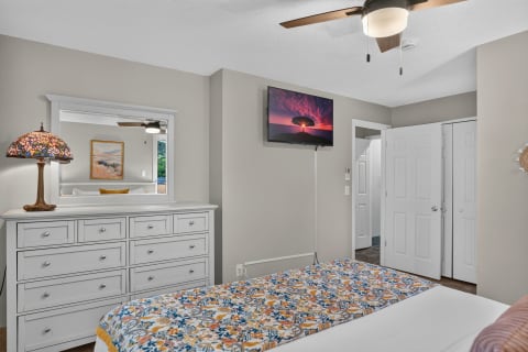 A cozy bedroom with gray walls, a colorful floral bedspread, a white dresser, and a mounted TV.