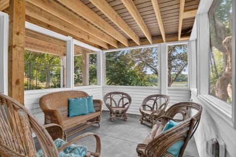 Cozy screened porch with wicker furniture and lush views outside.