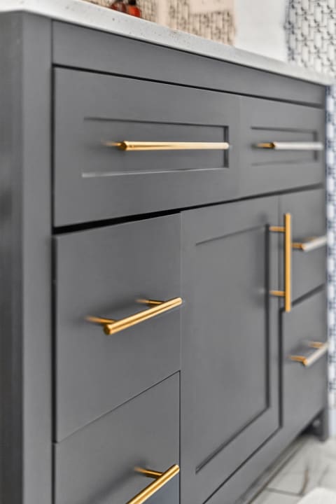 Close-up of sleek gray cabinetry with brass pulls and a light-colored countertop.