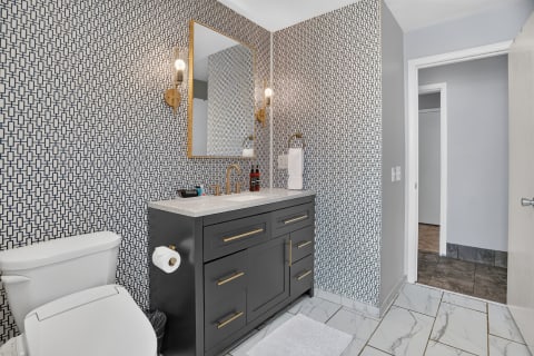Modern bathroom with geometric wallpaper, a dark vanity, and marble-look tile floor.