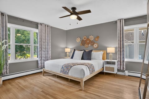 A modern bedroom with a king-size bed, hardwood floors, and large windows filling the space with light.