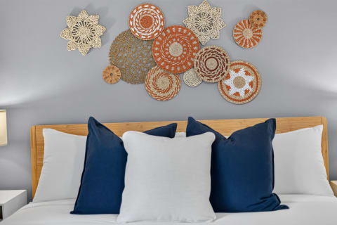 A stylish bedroom with handwoven baskets on the wall above a bed dressed in white linens and navy pillows.
