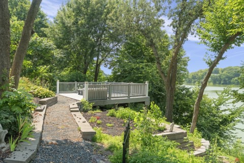 A peaceful deck overlooking calm lake waters, framed by trees and colorful garden flowers.