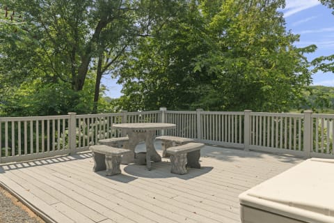 A cozy deck with a stone table and benches, surrounded by vivid green trees and a wooden railing.
