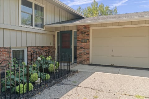 Welcoming home entrance with brick and siding, vibrant greenery, and an attached garage.