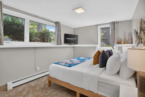 Modern bedroom with natural light, decorative pillows, and garden views through large windows.