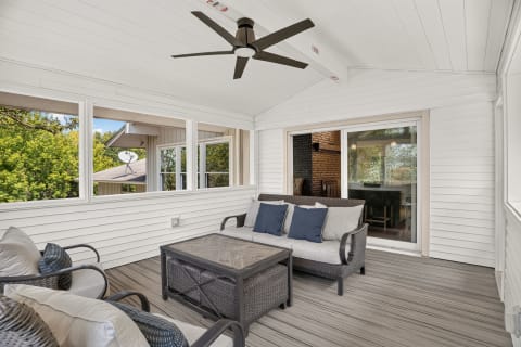 Screened porch featuring a sofa and chairs, large windows, and a ceiling fan.
