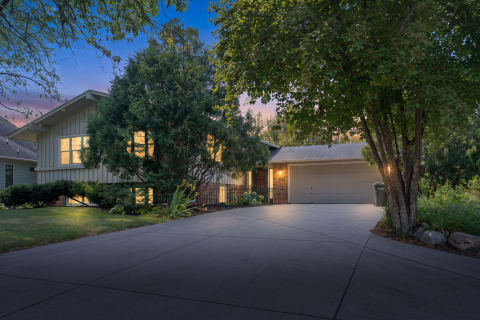 A residential house in a peaceful neighborhood with warm lighting and lush landscaping at dusk.