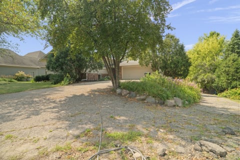 A single-story house in a quiet neighborhood with landscaped gardens and a gravel driveway under blue skies.