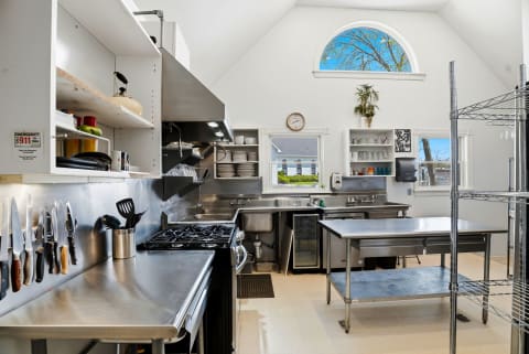 Your fully equipped professional-grade kitchen awaits with gleaming stainless steel surfaces, abundant workspace, and soaring ceilings that create a bright, inspiring space for preparing memorable meals together.
