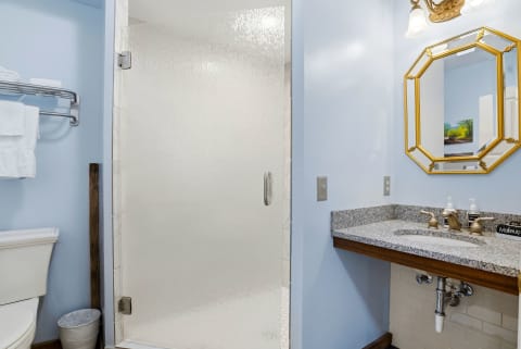 Your private bathroom features a spacious walk-in shower, elegant granite countertops, and thoughtful touches like fresh towels and a charming gold-framed mirror to help you feel right at home.