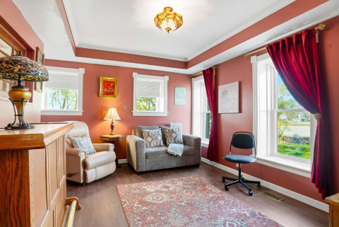 Settle into this inviting living space with warm terracotta walls, plush seating, and elegant touches. Large windows frame peaceful neighborhood views, while rich drapes add a cozy ambiance perfect for relaxing.