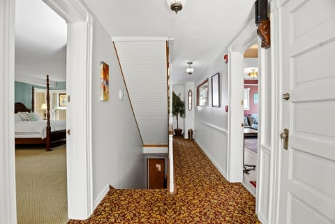 This bright upstairs hallway connects your private bedrooms, featuring classic wainscoting, warm lighting, and distinctive patterned carpeting that adds character throughout the second floor.