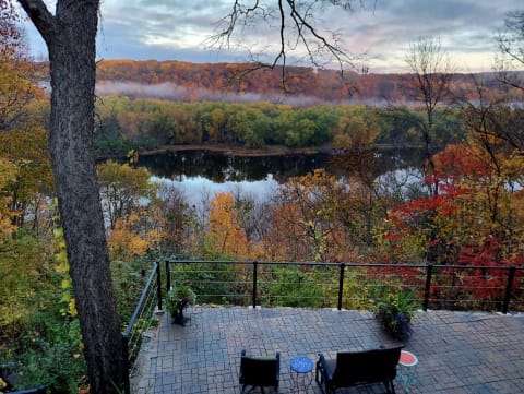 A stunning autumn view from a stone patio overlooking a river surrounded by colorful trees and misty hills.