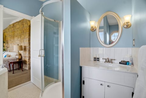 A bathroom with soft blue walls, a glass shower, and a marble vanity, blending vintage and modern styles.