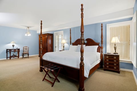 A spacious bedroom with a four-poster bed, light blue walls, and classic furnishings.