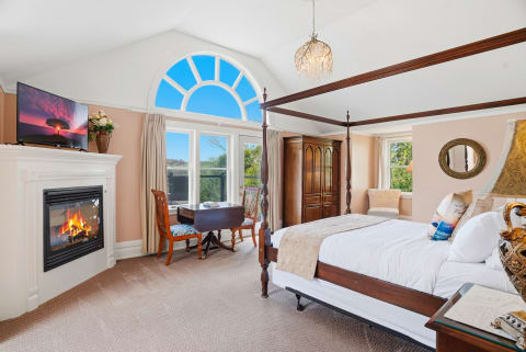 A sophisticated bedroom featuring a four-poster bed, fireplace, and large windows.