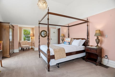 A beautifully furnished bedroom with a wooden canopy bed, vintage furniture, and peach walls.