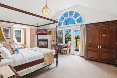 Elegant bedroom featuring a four-poster bed, fireplace, and large windows with a view.