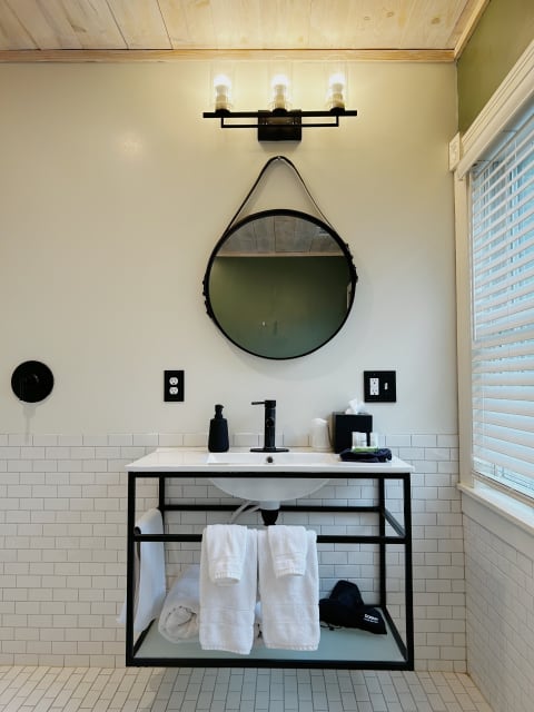 A modern bathroom with a black metal frame vanity, round mirror, and ample natural light.