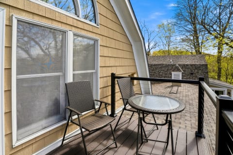 A balcony with two chairs and a table, surrounded by trees and rooftops.