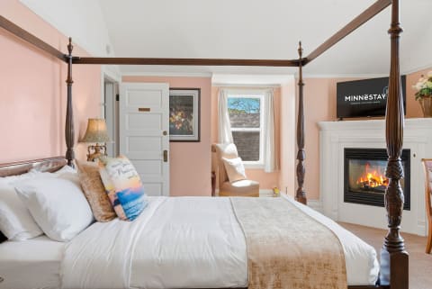A beautifully decorated bedroom featuring a four-poster bed, fireplace, and large window.