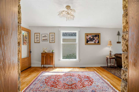 Step into a bright and welcoming living room where polished hardwood floors glow beneath the elegant chandelier. Vintage charm meets comfort with classic furnishings and natural light pouring through the window, creating your perfect retreat.