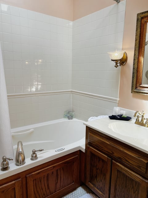 A bathroom featuring a jetted tub surrounded by white tile and rich wood cabinetry.