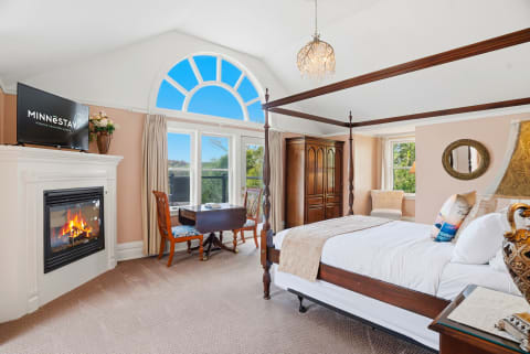 An elegant bedroom featuring a four-poster bed, a gas fireplace, and large windows.
